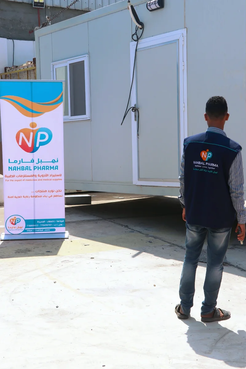 A Nahbal Pharma team member in front of the clinic unit's door, beside a company banner